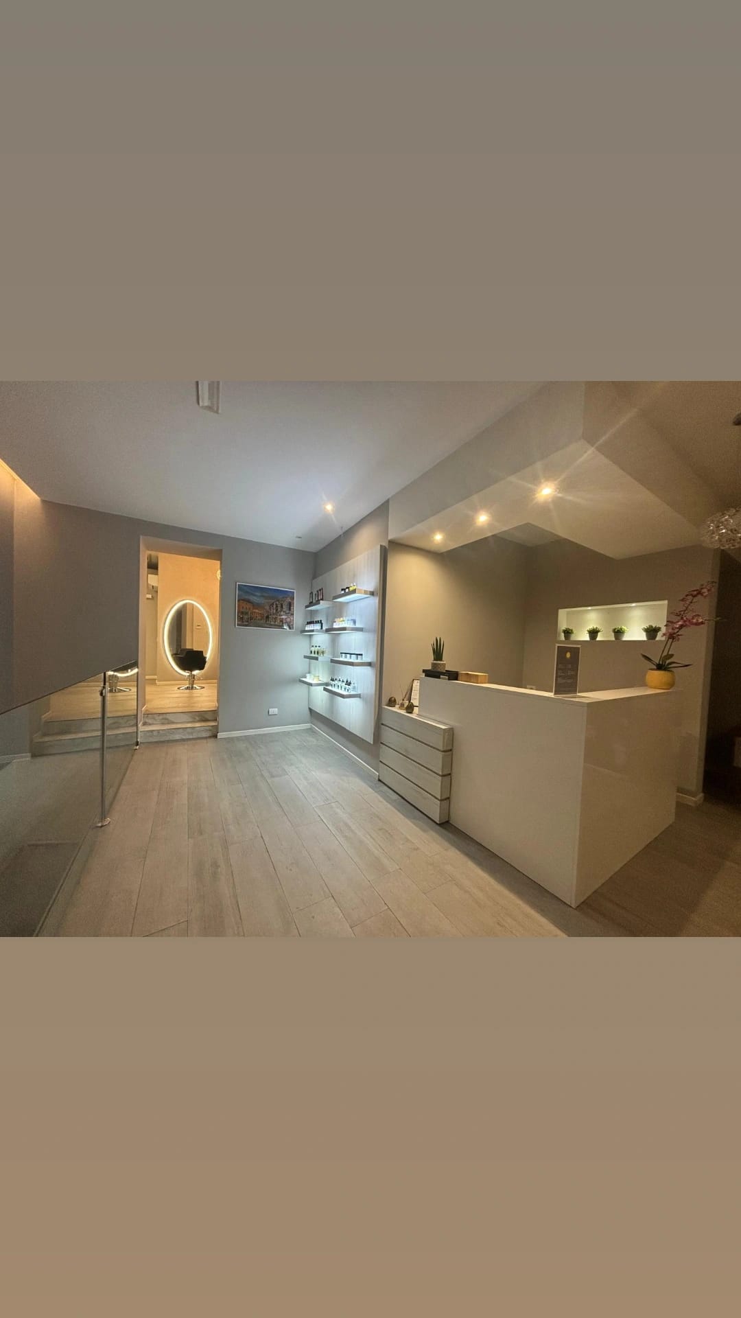 Wide view of a modern reception area with a counter, product shelving, doorway and wood-look flooring, lit by recessed ceiling lights.