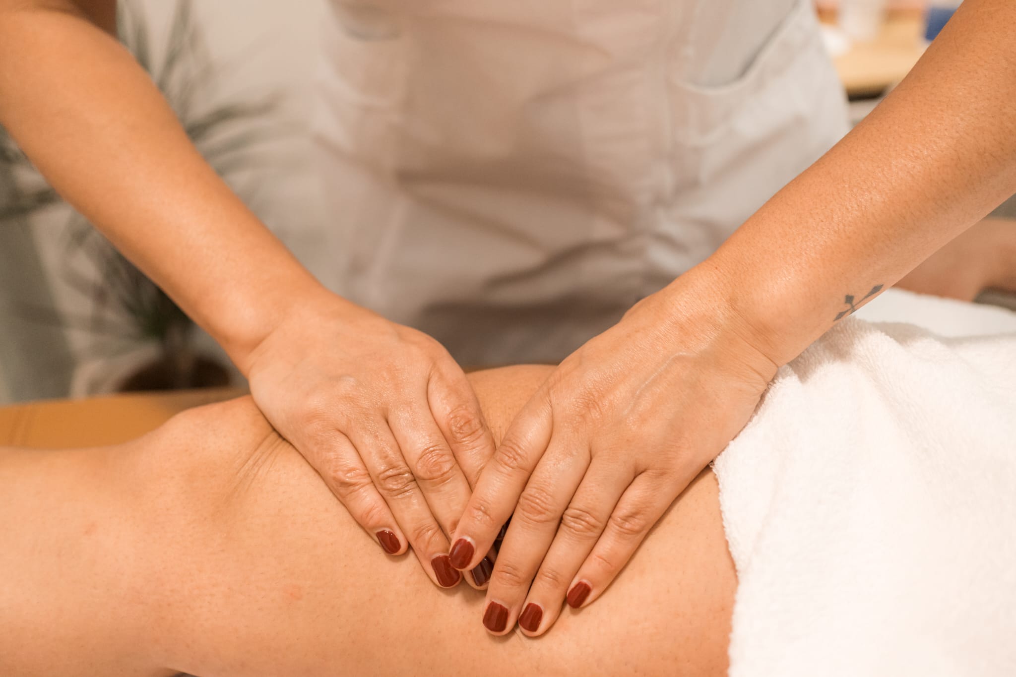 Close-up of hands applying pressure to a person’s lower back, with a white towel at the side and soft indoor lighting.