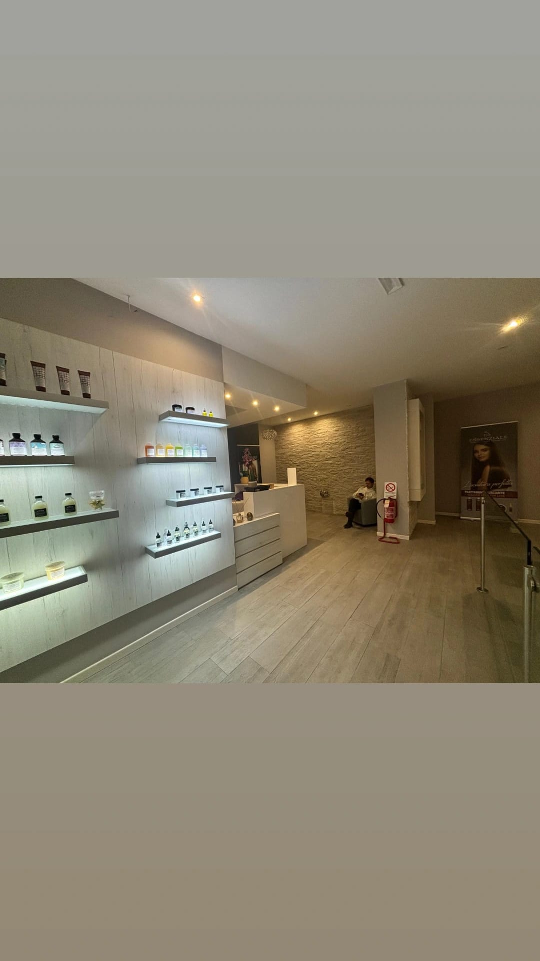 Wide salon interior showing illuminated product shelves, a reception counter, seating and wood-look flooring under warm ceiling lighting.