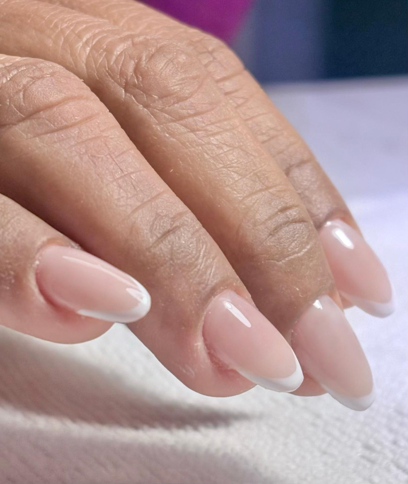 Close-up of a hand with glossy pale-pink French-tip nails resting on a softly lit white surface.